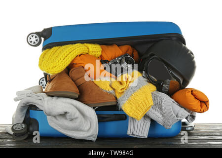 Koffer mit warmer Kleidung und Outfit auf hölzernen Tisch gegen weiße Hintergrund geöffnet. Winter Ferienhäuser Konzept Stockfoto