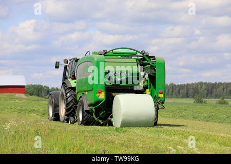 Salo, Finnland. Juni 15, 2019. Deutz-Fahr Schlepper und McHale 3 plus Pressen Pressen von Silage in grün Kunststoff Blatt im Heu Feld an einem sonnigen Tag im Sommer. Stockfoto