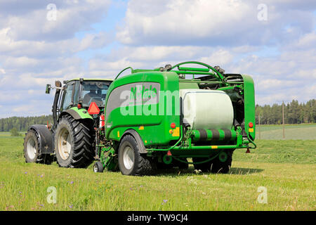 Salo, Finnland. Juni 15, 2019. Deutz-Fahr Schlepper und McHale 3 plus Pressen Pressen von Silage in grün Kunststoff Blatt im Heu Feld an einem sonnigen Tag im Sommer. Stockfoto