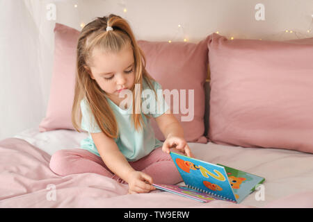 Süße kleine Mädchen lesen Buch beim Sitzen auf dem Bett zu Hause. Stockfoto