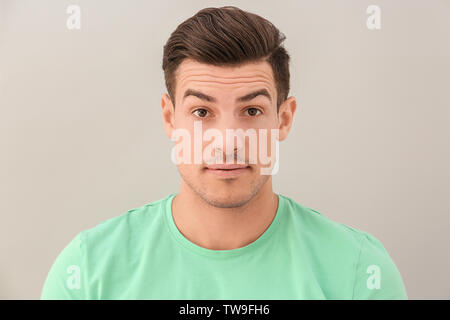 Junger Mann mit hochgezogenen Augenbrauen auf hellen Hintergrund Stockfoto