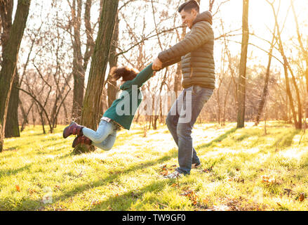 Junge Menschen spielen mit kleinen Mädchen im Freien an einem sonnigen Tag. Kind Annahme Stockfoto