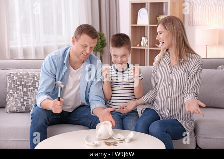 Glückliche Familie brechen Sparschwein mit Hammer zu Hause Stockfoto