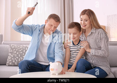 Glückliche Familie brechen Sparschwein mit Hammer zu Hause Stockfoto