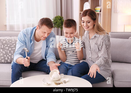 Glückliche Familie brechen Sparschwein mit Hammer zu Hause Stockfoto