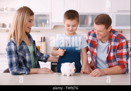 Glückliche Familie brechen Sparschwein mit Hammer zu Hause Stockfoto