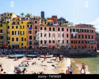 Gebäude in der Umgebung des Hafen von Vernazza und touristische Sonnenbaden an der Küste in der Region Cinque Terre. Vernazza, Italien - 20 April, 2019 Stockfoto