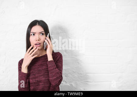 Emotionale junge Frau Gespräch am Handy in der Nähe von weißen Wand Stockfoto