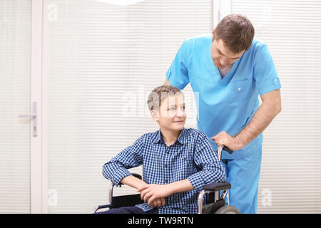 Männlicher Arzt darauf achten, dass der kleine Junge im Rollstuhl im Innenbereich Stockfoto