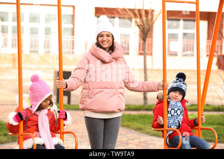 Junge Frau mit kleinen Kindern auf dem Spielplatz. Kind Annahme Stockfoto