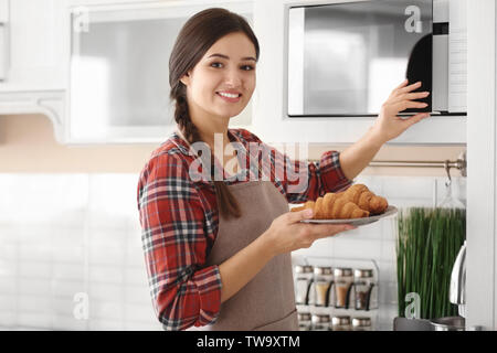 Frau setzenden Platte mit Croissants in der Mikrowelle im Innenbereich Stockfoto