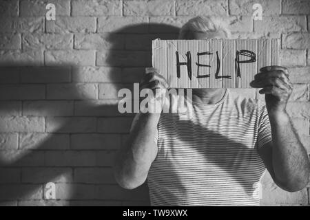 Armer Mann Holding mit Wort HILFE auf Mauer Hintergrund. Schwarzweiß-Effekt Stockfoto