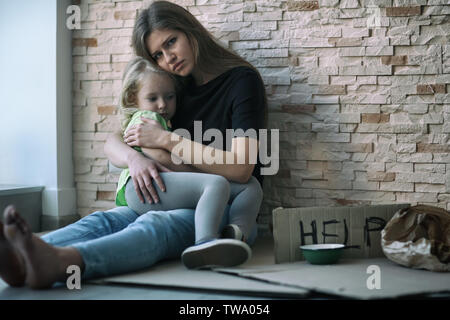 Obdachlosen armen Frau und ihre kleine Tochter sitzen in der Nähe von Mauer und um Hilfe zu bitten Stockfoto