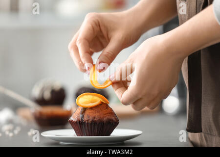 Frau dekorieren lecker Kuchen mit Orangenscheiben am Tisch Stockfoto