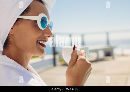 In der Nähe der schöne junge Frau am Pool/in. Weibliche Modell tragen Bademantel und Sonnenbrille entspannen im Resort. Stockfoto