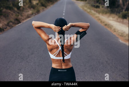 Ansicht von hinten erschossen der muskulöse Frau ihr Haar binden und für einen Sprint bereit. Fitness Frau vor einem Ansturm auf die leere Straße. Stockfoto