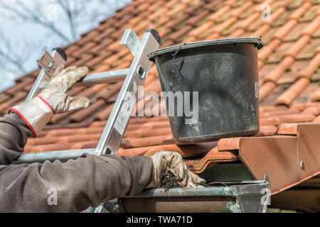 Mann auf einer Leiter Reinigung Haus Dachrinnen Stockfoto