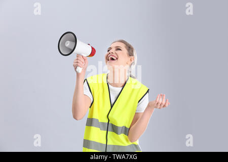 Junge Frau in reflektierende Weste mit Megafon auf grauem Hintergrund Stockfoto