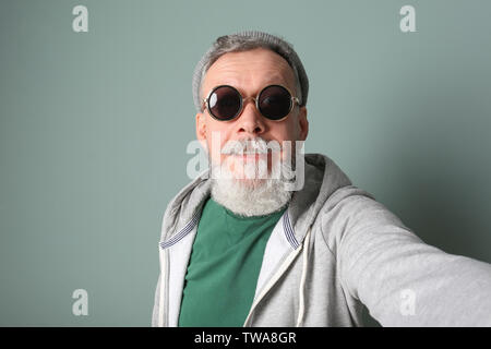 Gerne älterer Mann in hipster Outfit unter selfie auf grauem Hintergrund Stockfoto