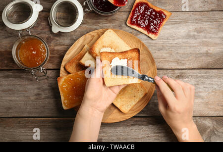 Frau Verbreitung Butter auf geröstetem Brot über Tabelle, Ansicht von oben Stockfoto