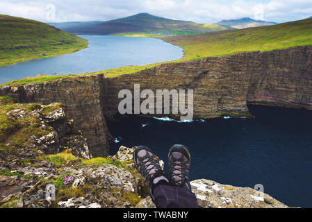 Beine der Wanderer sitzen auf einer Klippe über dem See Sorvagsvatn auf den Färöer Inseln Stockfoto