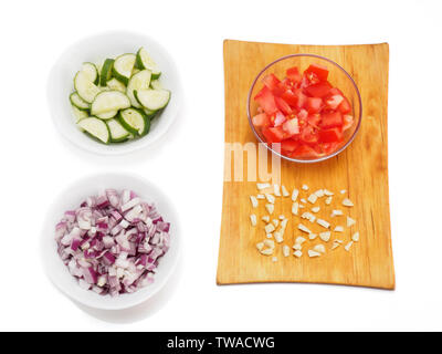 In Scheiben geschnittene Tomaten in einem transparenten Schüssel und gehacktem Knoblauch auf einem Schneidebrett. Weißer Hintergrund. In Scheiben geschnittenen roten Zwiebeln und Gurken in einer weißen Schüssel Stockfoto