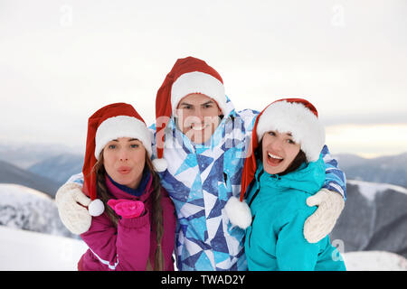 Gerne Freunde in Santa Hüte auf verschneiten Berggipfel im Resort. Winterurlaub Stockfoto