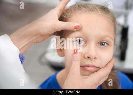 Nahaufnahme der Mädchen an der Kamera suchen, während die weiblichen Augenarzt prüfen Vision in der Klinik. Kind mit blauen Augen sitzen in optischen Speichern, während Arzt auf Augenhöhe Schüler suchen. Konzept der medizinischen Untersuchung. Stockfoto