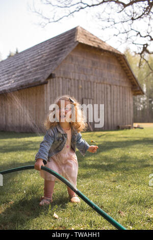 Schönes, glückliches Mädchen mit lockigem Haar, in Sommer Spaß, schreien in der Aufregung, Spielen im Freien mit Wasser besprüht aus Gartenschlauch Stockfoto