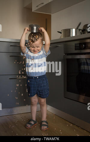 Little Boy In strömen Bündel getrocknete Bohnen über seinen Kopf, aus Edelstahl Schüssel, in einem grauen Küche Stockfoto