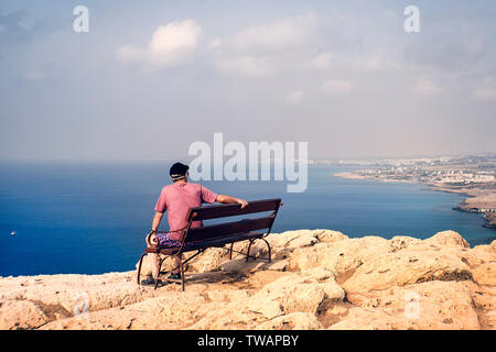Nicht identifizierten männlichen Erwachsenen auf einer Bank sitzen und die Aussicht auf die Berge, die Stadt in der Ferne und die Bucht genießen. einsamen alten Mann. Konzept der Verlust, Sor Stockfoto