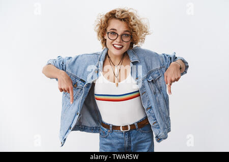 Verpassen Sie nicht die Chance, zu prüfen cool Promo. Portrait von begeisterten gut aussehende stilvolle blonde Frau mit kurzen Haarschnitt in Jeans Jacke und Brille Stockfoto