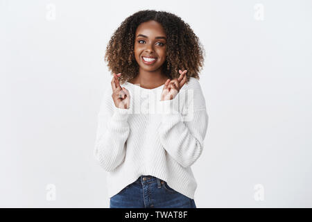 Charmantes, freundliches, gut aussehende African American Curly - behaarte Frau betet für gutes Glück cross Finger lächelnd Vorfreude, supplicating wanna Traum Stockfoto