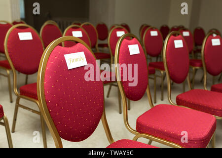 Sitzmöbel Stühle für Gäste einer Hochzeit im Festsaal. Stühle mit im roten Tuch Typenschild Familie. Stockfoto