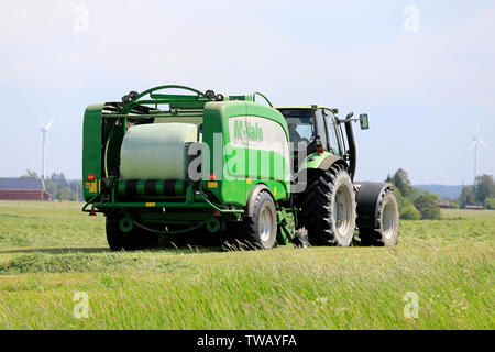 Salo, Finnland. Juni 15, 2019. Deutz-Fahr Schlepper und McHale 3 plus Pressen Pressen von Silage in grün Kunststoff Blatt im Heu Feld an einem sonnigen Tag im Sommer. Stockfoto