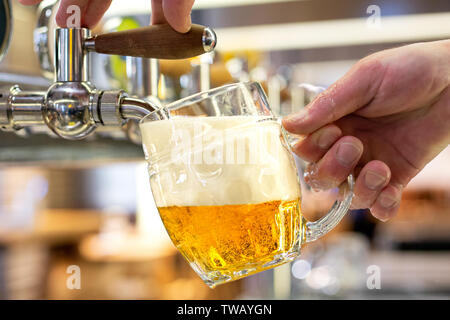 Ein Mann gießen Fass Bier in eine genoppte Glas Becher in ein modernes Pub. Stockfoto