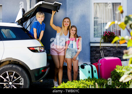 Mutter, Mädchen und Jungen laden bunte Koffer in den Kofferraum des Autos. Familie mit Hund Labrador stand in der Nähe des Auto und für die Reise fertig. Stockfoto