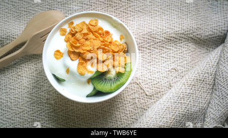 Corn flakes, Müsli und Milch Spritzen in der Schüssel. Natürliche selbstgemachte Plain organischen Joghurt in Holz Schüssel auf Holz Textur Hintergrund Stockfoto