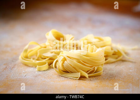 Frische Fettuccine Pasta nisten auf einem Holztisch mit Mehl Stockfoto