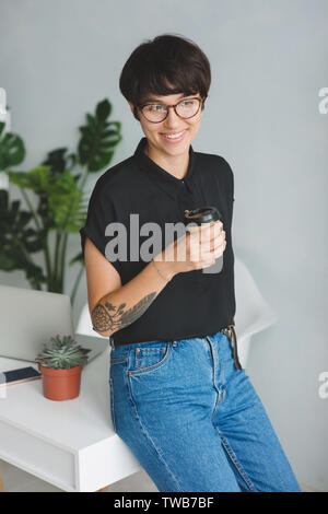 Portrait Of Smiling Pretty Young Business Woman in Gläsern mit Kaffee zu sitzen am Schreibtisch. Stockfoto