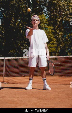 Tennis Sport. Man Tennis Spielen im Freien. Portrait von attraktiven jungen Mann im weißen T-Shirt mit Schläger und Ball am Himmel Hintergrund. Aktiven Lebensstil Stockfoto