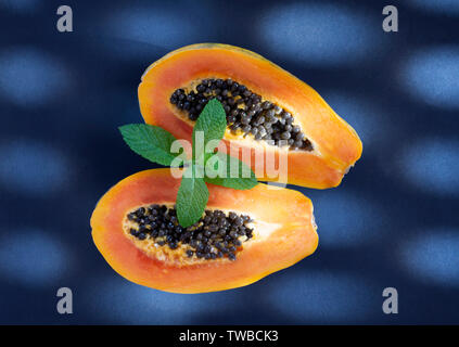 Papaya auf blauem Hintergrund mit Beleuchtung aus einem blinden Fenster Stockfoto