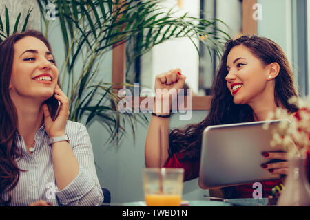 Zwei aufgeregt weibliche Freunde feiern Erfolg Lesen gute Nachrichten ion Digital Tablette im Cafe. Stockfoto