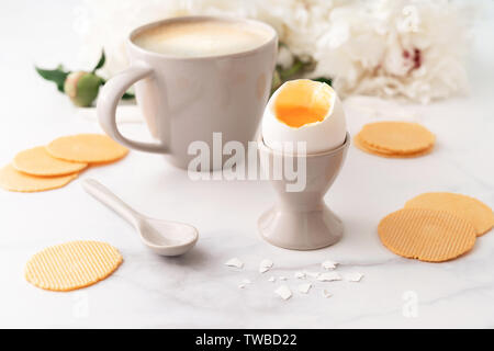 Weich gekochte Ei mit liquide orange Eigelb in Keramik Eierbecher, Tasse Kaffee mit keramischen Löffel und dünne knusprige Mais Chips auf dem Hintergrund der schönen wh Stockfoto
