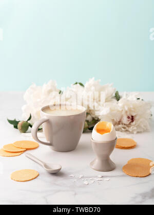 Weich gekochte Ei mit liquide orange Eigelb in Keramik Eierbecher, Tasse Kaffee mit keramischen Löffel und dünne knusprige Mais Chips auf dem Hintergrund der schönen wh Stockfoto