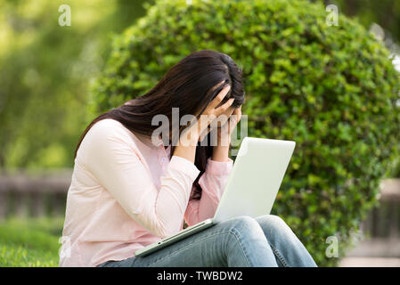 Junge schöne Frau im Freien in einem öffentlichen Park. Arbeiten am Laptop im Freien. Zugeschnittenes Bild der weiblichen Arbeiten am Laptop während der Sitzung in einem Park. Stockfoto