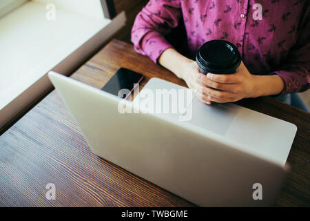 Überblick über eine junge Frau in einem Cafe vor dem Laptop sitzen, eine Tasse Kaffee. Smartphone Neben. Stockfoto