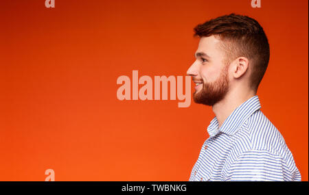 Seitenansicht Portrait von lächelnden tausendjährigen Mann weg bei copy Space auf orangem Hintergrund, Panorama Stockfoto