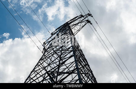 Ansicht von unten auf eine hohe Spannung Strom pylon gegen den blauen Himmel mit Wolken am sonnigen Tag. Hochspannungsnetzteil Sendeturm. Power Engineering. Stockfoto