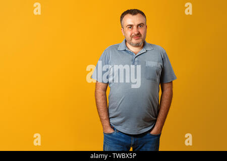 Stattlicher Mann mit Händen in den Taschen auf gelben Hintergrund, an der Kamera schaut. Happy Guy lächelt. Stockfoto